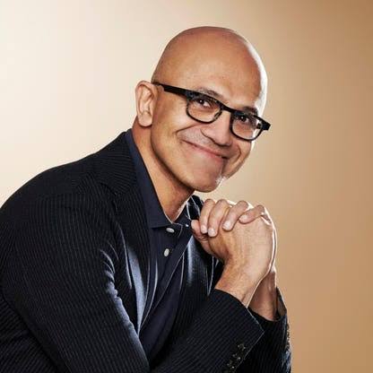 Portrait of Microsoft CEO Satya Nadella smiling against a warm studio backdrop.