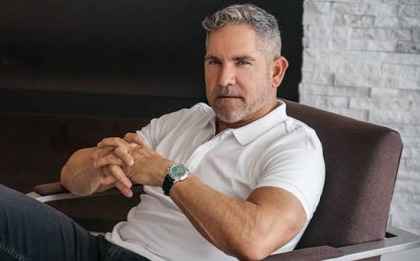 Grant Cardone seated in a chair wearing a white polo shirt and a watch.