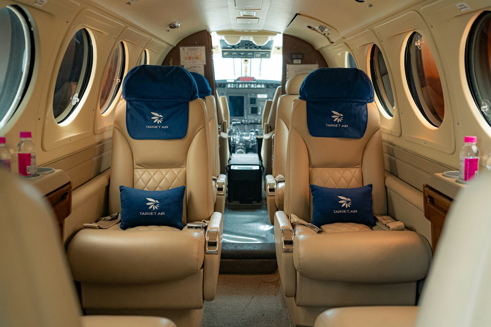 Interior view of an empty private jet cabin with cream leather armchairs and a wood table.