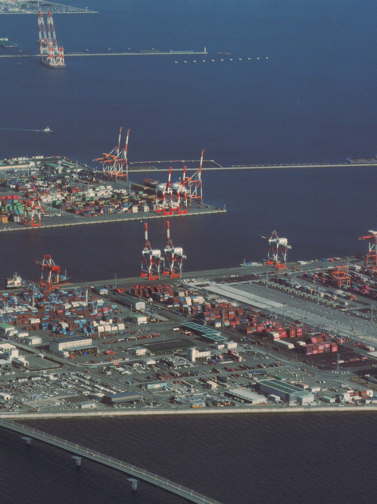 Aerial view of stacked shipping containers and gantry cranes at a shipping port at sunrise.